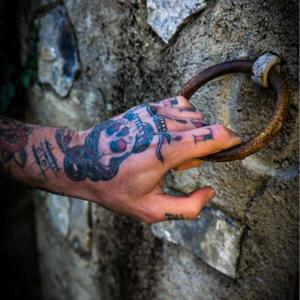 Bold Traditional Style Skull with a Snake wrapped around its Head Top of Hand Tattoo | selftattoo.com