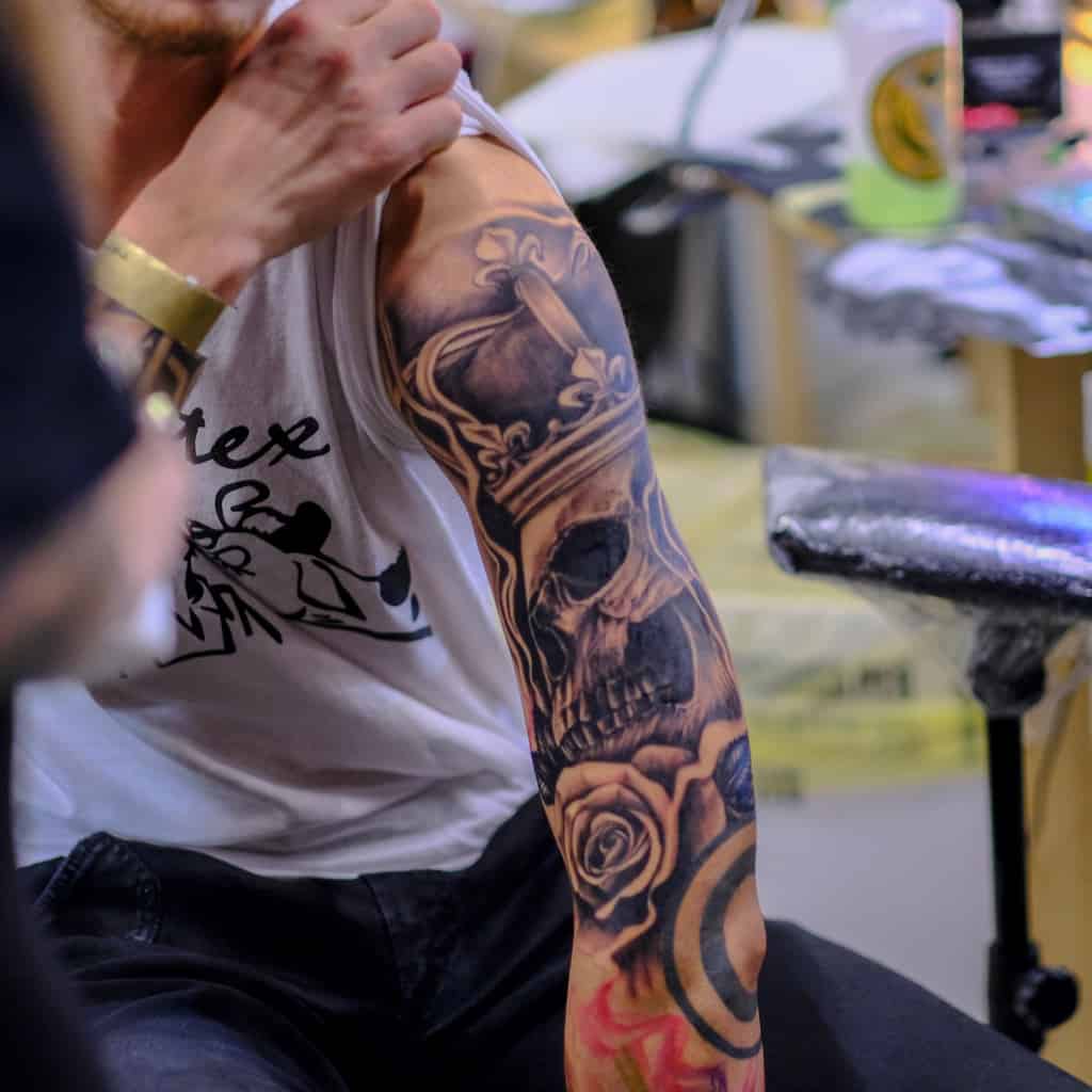 Hyper Realistic Black and Gray Skull wearing a Crown and Laying on a Rose Upper Arm Tattoo | selftattoo.com