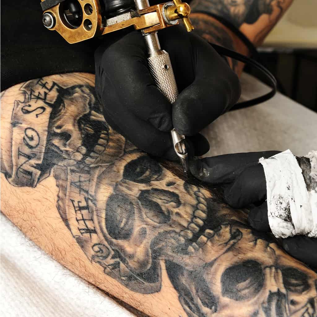 Three Realistic Black and Gray Skulls on top of each other with Banners Upper Arm Tattoo | selftattoo.com