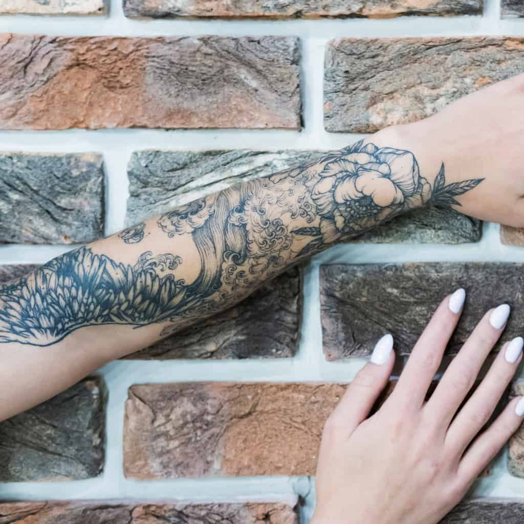 Detailed Fine Line Black and Gray Forearm Tattoo featuring a Flower and Wings surrounded by Waves | selftattoo.com