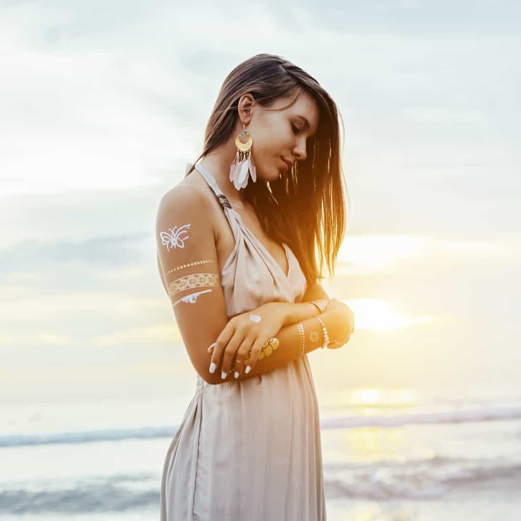 Woman Standing on a Beach with Gold Temporary Tattoos of a Butterfly and Geometric Patterns | selftattoo.com