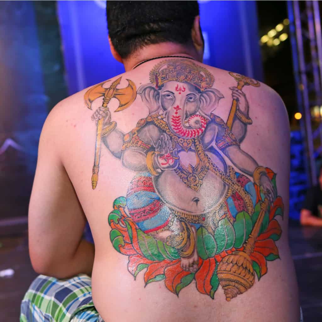 Colorful Hindu Deity Ganesha sitting on a Lotus Flower holding Symbolic Objects Full Back Tattoo | selftattoo.com