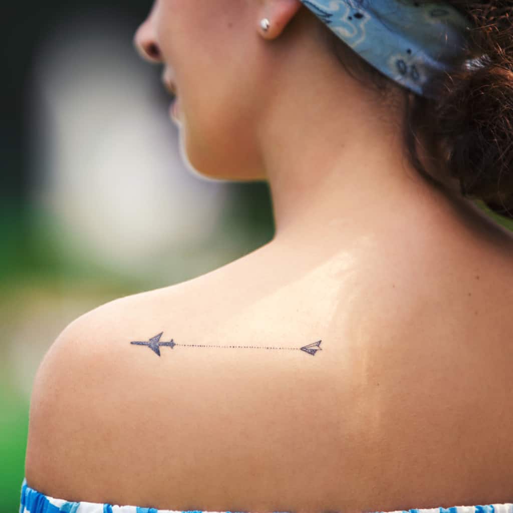 Small Minimalistic Black Paper Airplane with a Dashed Line leading to an Airplane Shoulder Tattoo | selftattoo.com