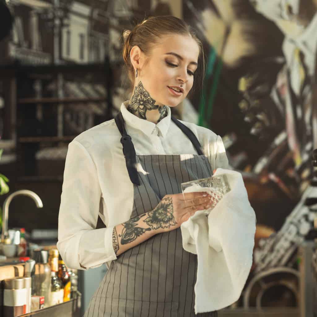 Bartender with Bold Black and Gray Tattoos on her Neck and Forearm | selftattoo.com