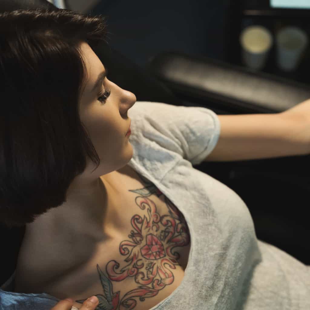 Central Jewel Heart surrounded by Scrolling Patterns colored in Red and Pink Upper Chest Tattoo | selftattoo.com