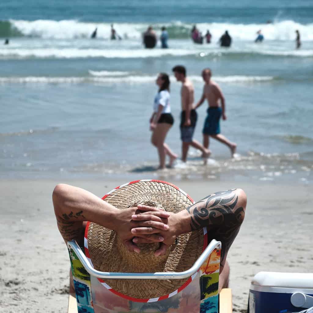 Man Lounging at the Beach with Bold Solid Black Tribal Style Sleeve Tattoo | selftattoo.com