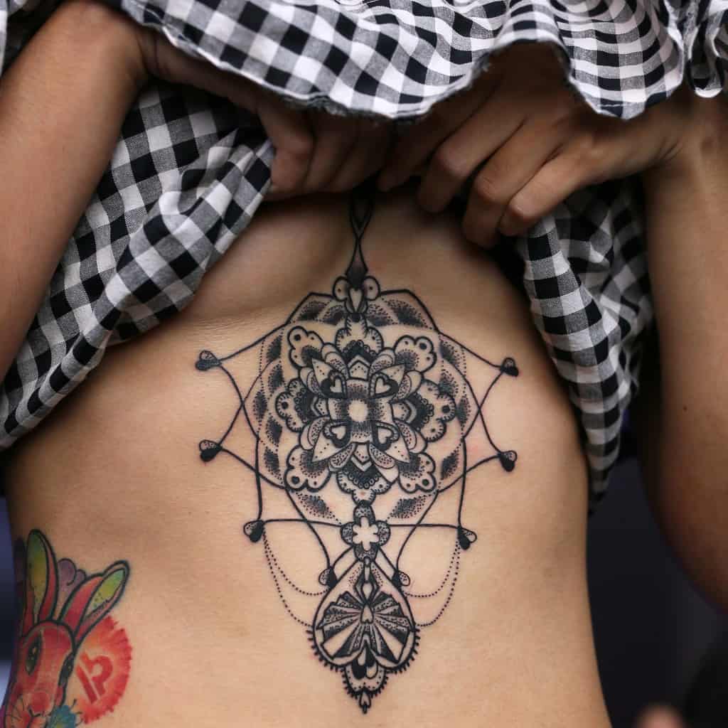 Bold Black Central Mandala Linework Sternum Tattoo with Dot Shading and a Hanging Pendant | selftattoo.com