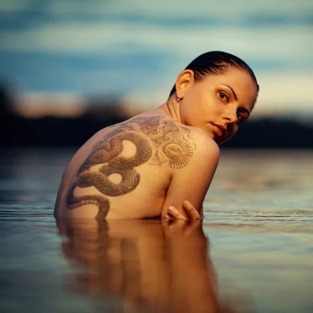 Large Realistic Black and Gray Coiled Snake next to Decorative Fine Line Patterns Back Tattoo | selftattoo.com
