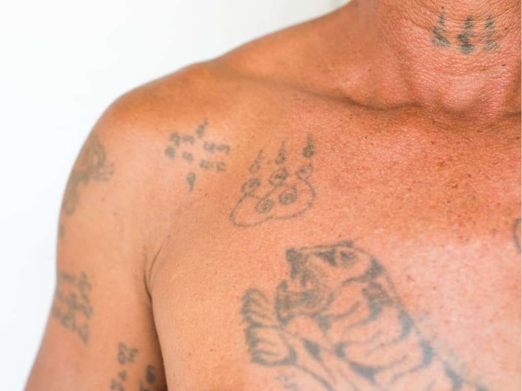 Faded Black Traditional Sak Yant Tattoos of a Tiger and Small Symbols/Script | selftattoo.com