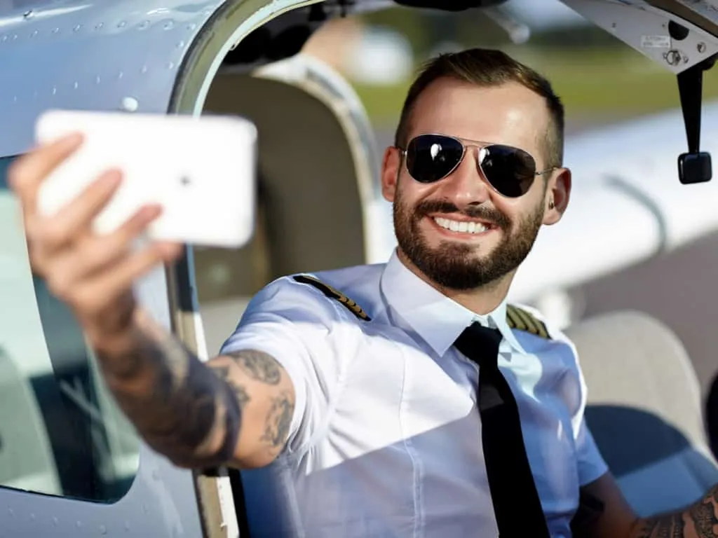 A Pilot taking a Selfie in front of an Airplane with a visible Sleeve Tattoo | selftattoo.com