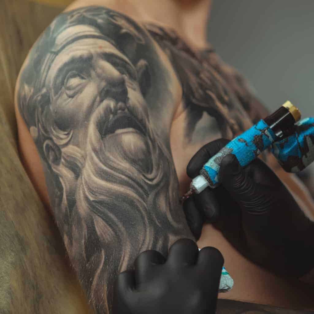 Hyper Realistic Black and Gray Portrait Arm Tattoo of a Greek/Roman Figure with Long Flowing Beard | selftattoo.com