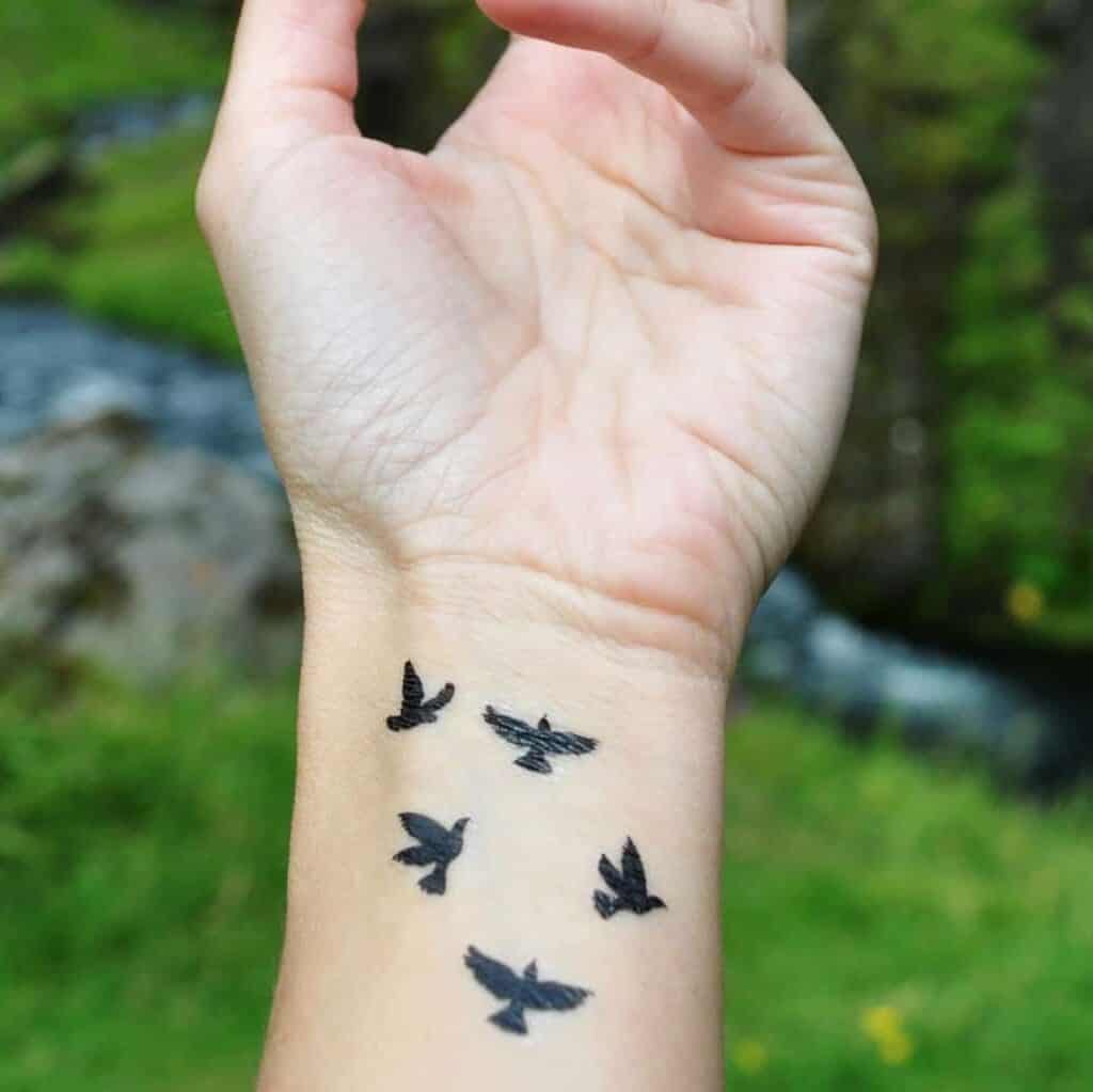 Five Small Black Silhouettes of Birds Wrist Tattoo | selftattoo.com